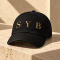 Wordmark Cap in black on limestone, showing Old Gold SYB flat embroidery and curved visor.