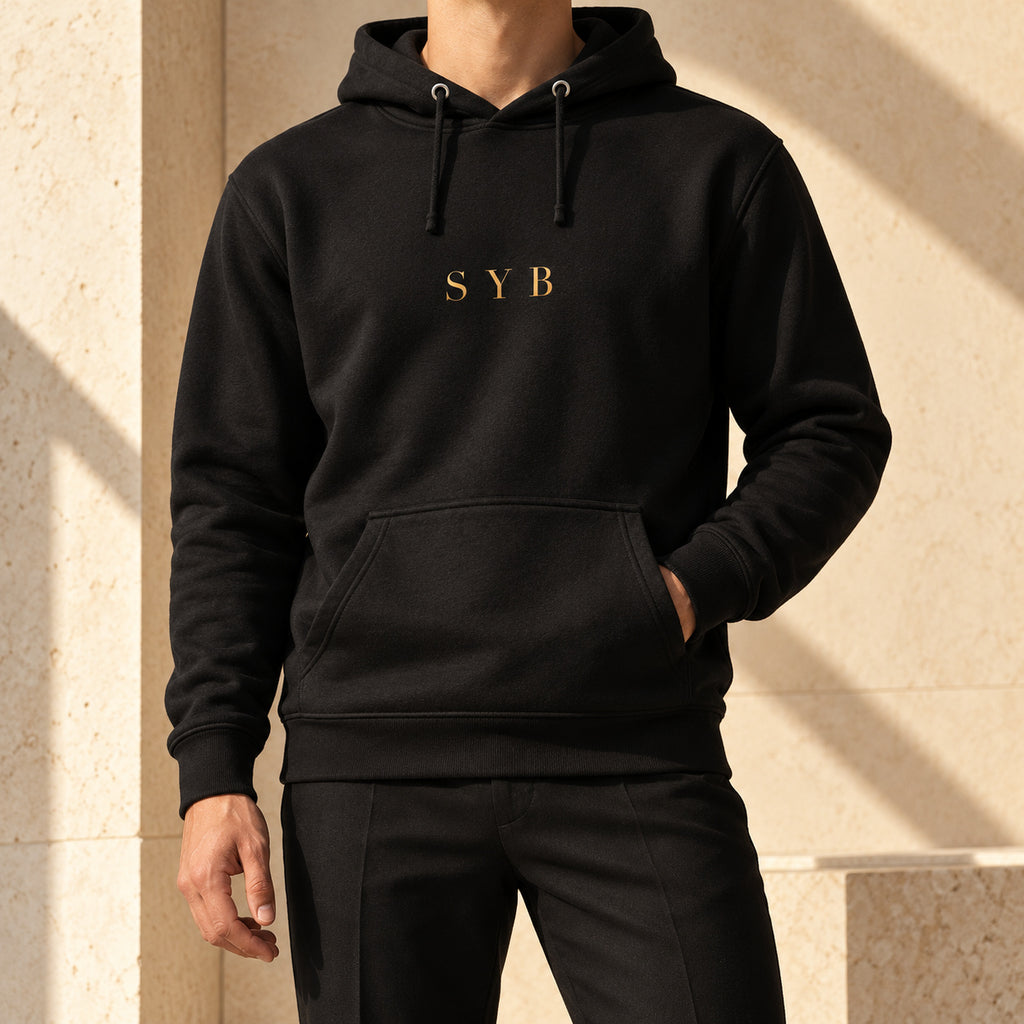 Wordmark Hoodie in black, styled with tailored trousers; small gold-tone SYB print and front pouch.