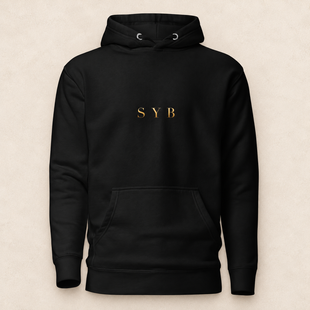 wordmark hoodie in black with original SYB gold artwork on a pale limestone studio background